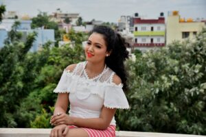Home A cheerful woman sitting outdoors in a white lace top against a cityscape backdrop.