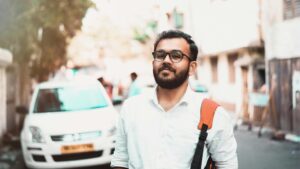 Home Confident man with glasses and backpack on a sunny urban street with cars in the background.